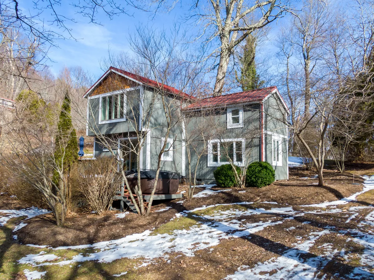 This exterior image highlights the house nestled among trees, with the private hot tub clearly visible on the deck, inviting relaxation amid a peaceful natural setting. The view gives a sense of the surrounding yard and tranquility of the valley location.