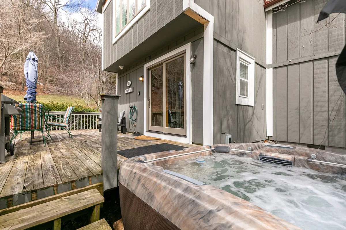 A spacious deck with a hot tub, comfortable outdoor seating, and lush natural surroundings. The scene suggests opportunities for relaxation, entertaining guests, or simply enjoying nature from the comfort of home.