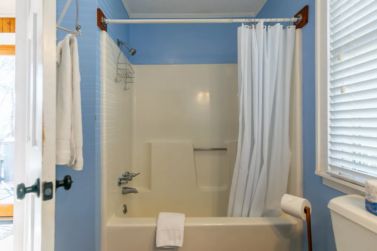 A bright, neatly maintained bathroom featuring a bathtub with a shower curtain, fresh towels, a sink, and well-organized amenities. The scene suggests comfort and convenience for guests after a long day in the mountains.