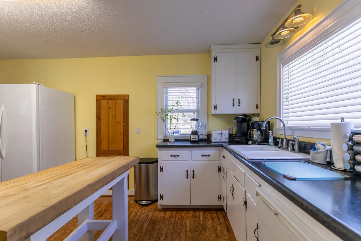 A bright, well-equipped kitchen featuring a central island, lush green plants on the window sill, and a cozy, welcoming ambiance. The scene hints at culinary creativity, with ample space for group meal prep or casual gatherings.