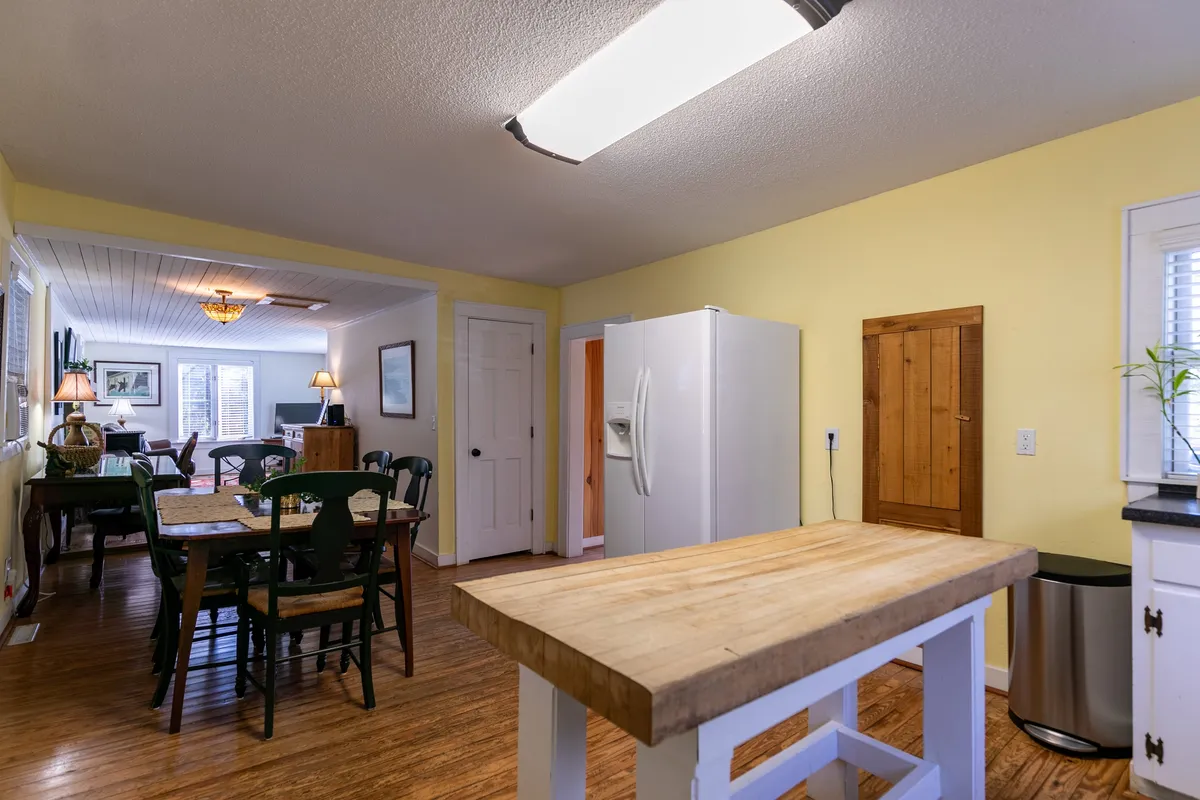 A warm and welcoming kitchen scene with a wooden kitchen island, green dining chairs, and a white refrigerator. The space encourages family gatherings, meal preparation, and shared experiences.