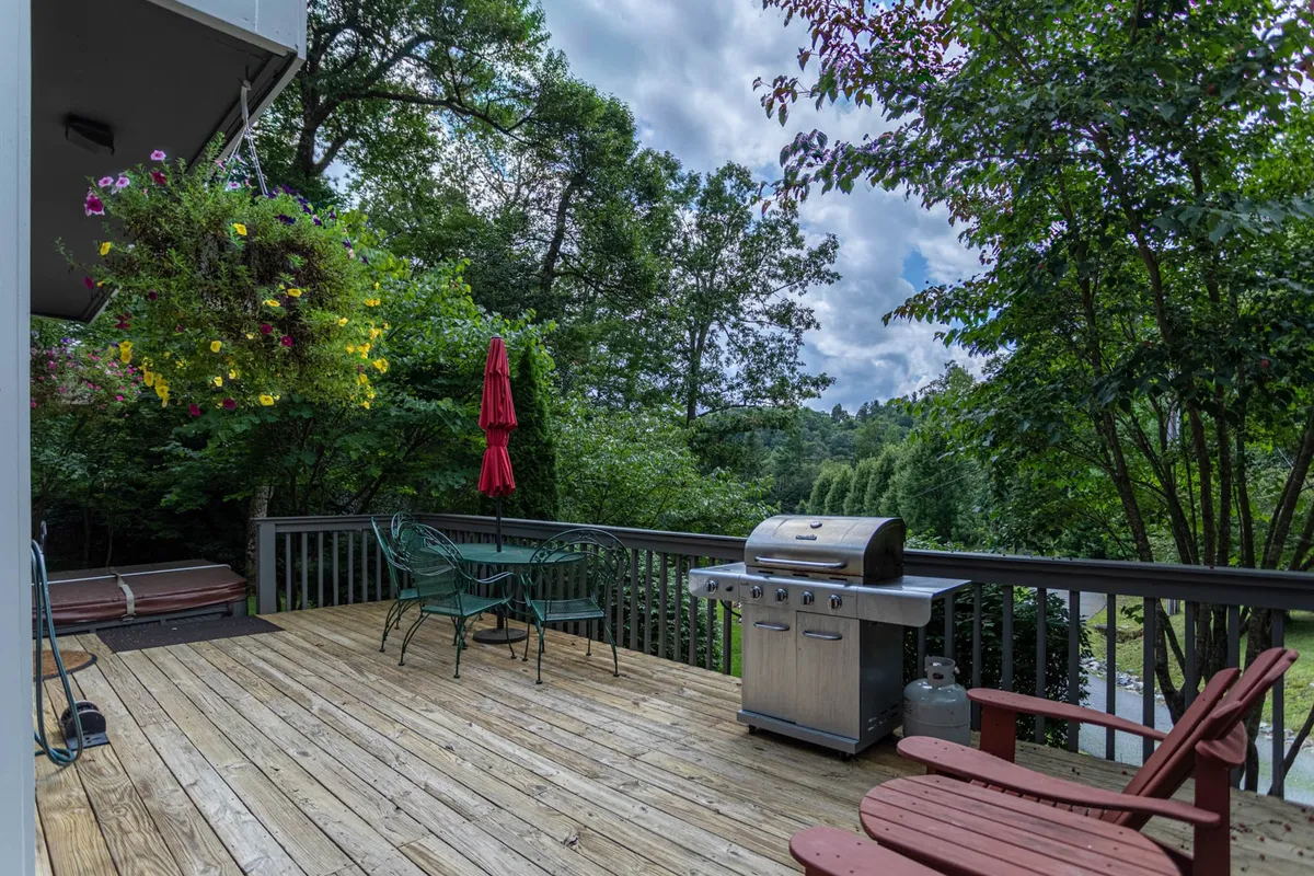This exterior image features a grill, red umbrella, outdoor seating, and hanging flowers on a welcoming deck. It captures the social aspect of evenings spent grilling, gathering, and enjoying meals outside with friends and family.