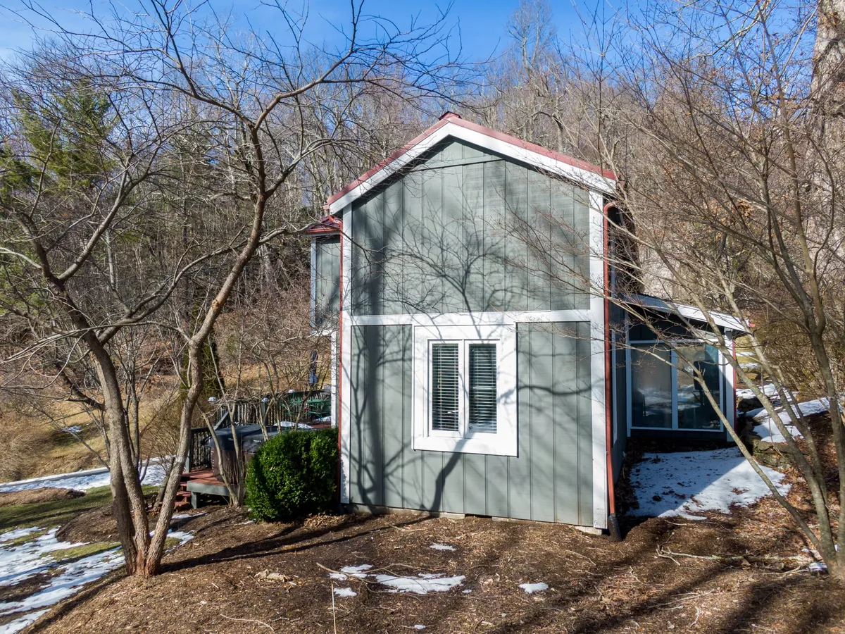 A tranquil view of the house surrounded by trees, with patches of snow visible, suggesting a seasonally dynamic landscape. The scene evokes the peace and beauty of mountain conditions, especially in winter.